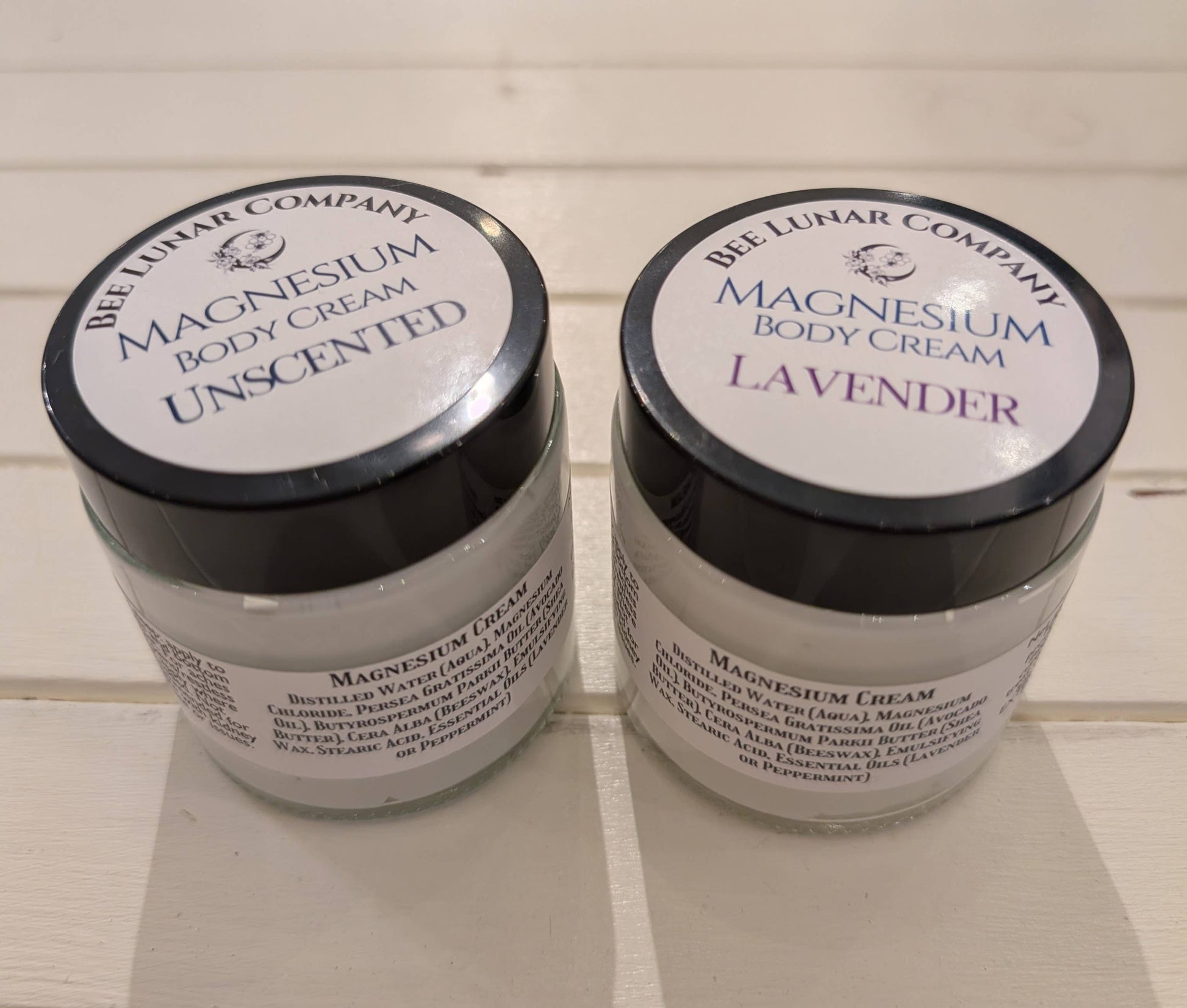 Two jars of magnesium body cream from the Bee Luhar Company on a tiled floor.