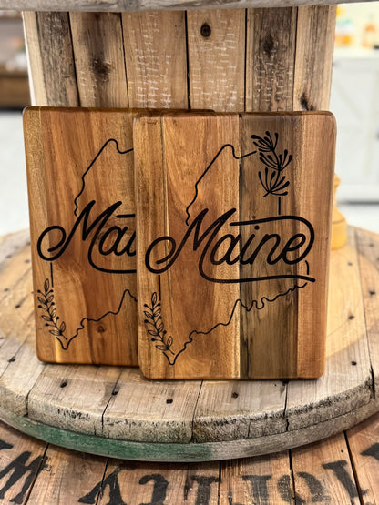 Two wooden cutting boards with 'Maine' engraving on a rustic wooden surface.